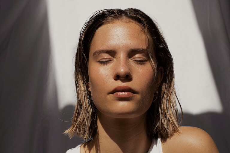 Das Gesicht einer jungen Frau, der die Sonne auf die Haut scheint